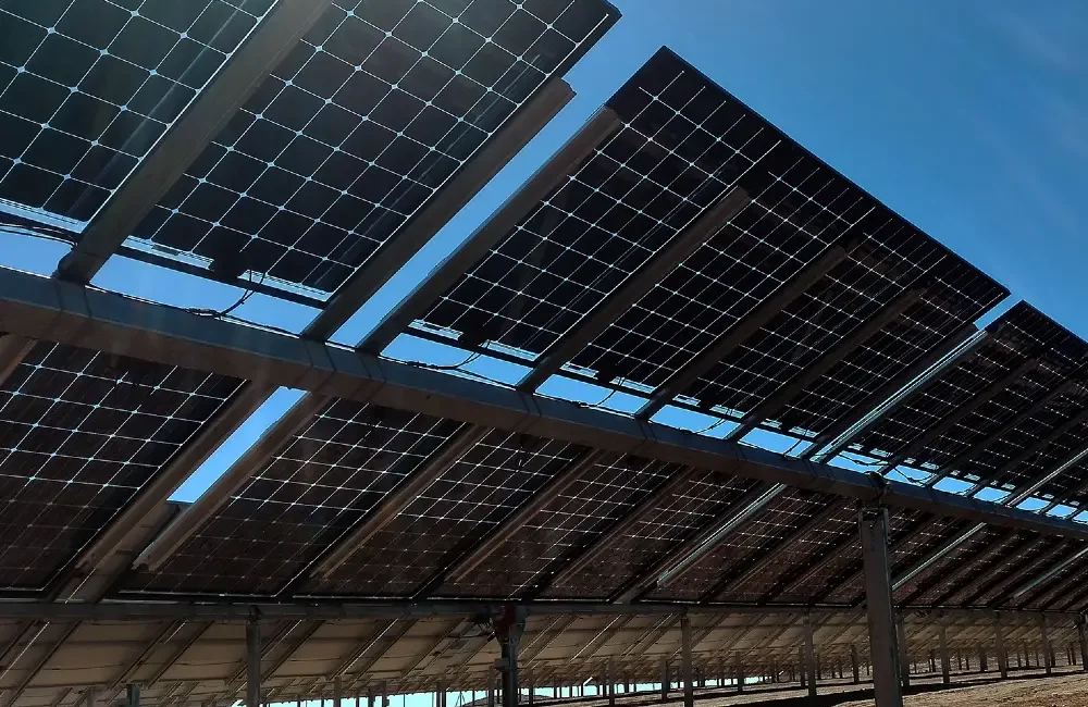 Bifacial solar panels mounted on an elevated ground-mounted structure in a dry Namibian environment with reflected sunlight visible beneath the modules