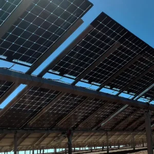 Bifacial solar panels mounted on an elevated ground-mounted structure in a dry Namibian environment with reflected sunlight visible beneath the modules